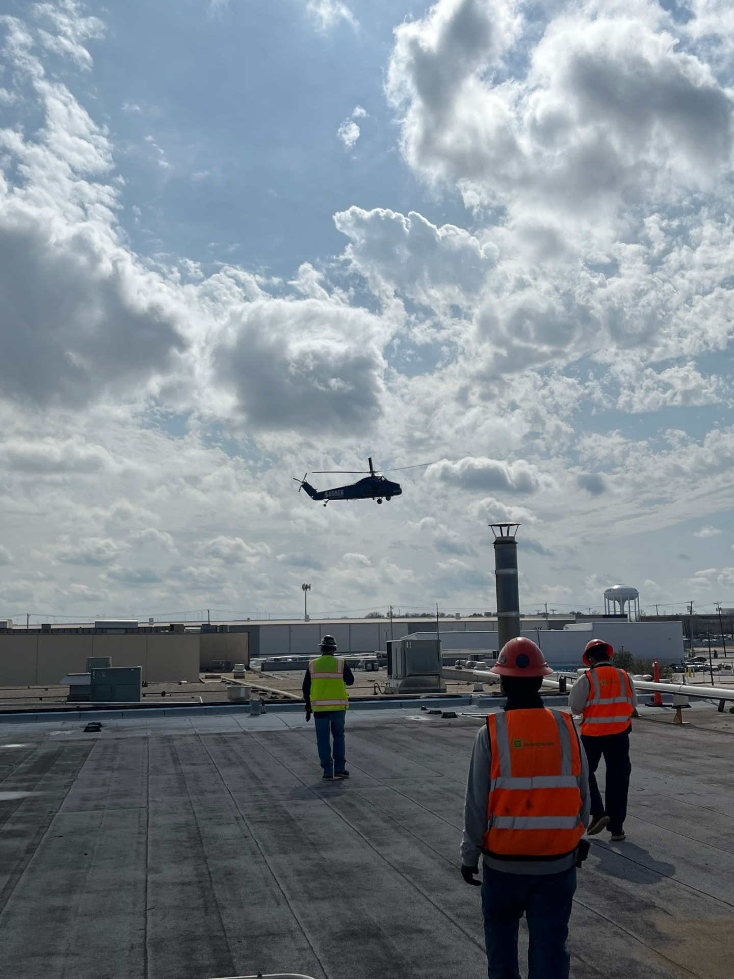Crew in high-visibility vests on a commercial rooftop as a helicopter sets equipment