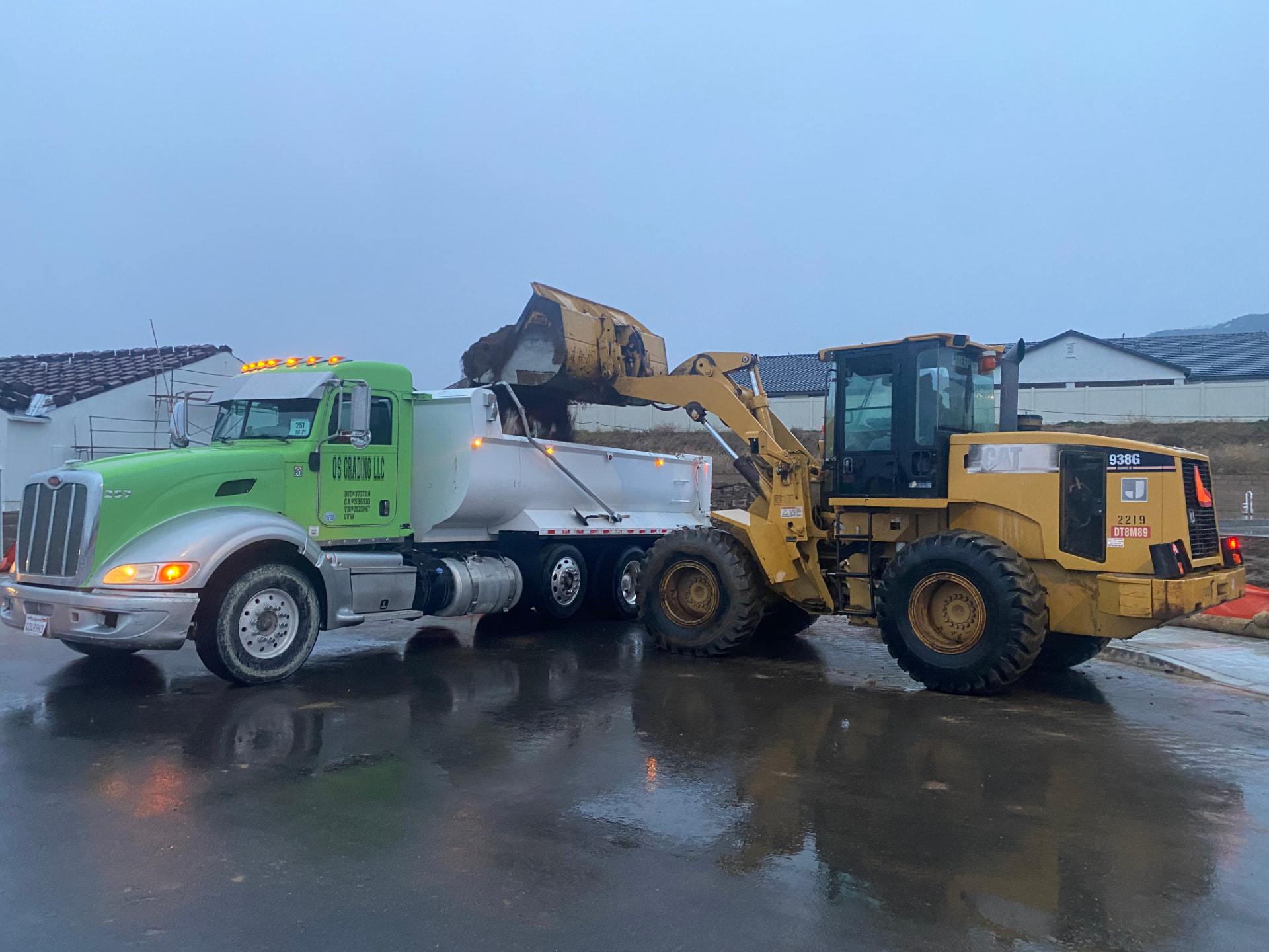 CAT 938G wheel loader loading an OS Grading dump truck at dawn in the rain