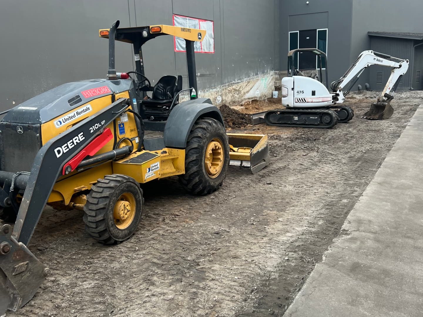 John Deere loader and Bobcat mini excavator performing sitework along a new commercial building